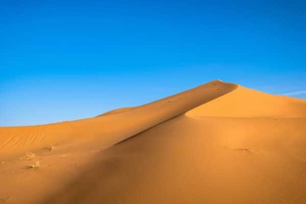 Femme musulmane non visible, dunes de sable au coucher du soleil, paysage désertique source d’inspiration pour la mode pudique Ynes Boutique.